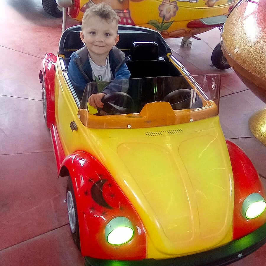 Tiago a rejoint le concours — aidez-le/la à gagner de superbes lots ! amusement_ride, child, clothing, colorful, entertainment, face, floor, fun, happy, head, indoor, light, playful, seat, small_car, smiling, steering_wheel, toy_car, vehicle, young_boy