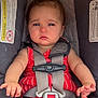 baby, car_seat, child, infant, safety_harness, red_clothing, blue_eyes, straps, black_socks, serious_expression, indoors, closeup, person, seat, child_safety, cute, small_hands, young_child, transportation, infant_clothing