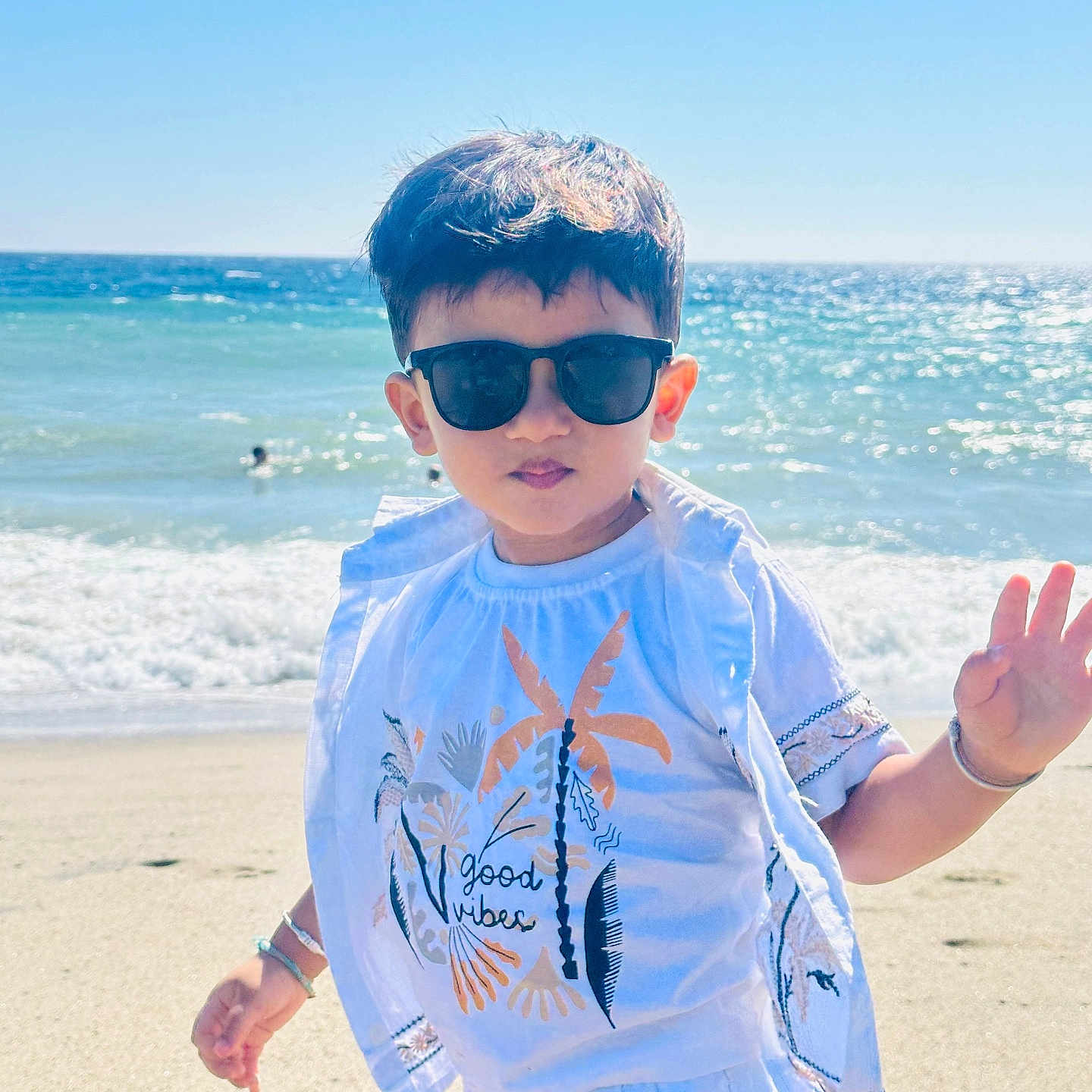Yuvaan is registered to the contest to win money with this photo: child, beach, ocean, seaside, sand, waves, sunglasses, smiling, waving, outdoors, summer, sunlight, portrait, standing, vacation, travel, water, sky, t_shirt, good_vibes