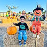 Yuvaan joined the competition — help win amazing prizes! child, toddler, smiling, portrait, halloween, pumpkin, scarecrow, hay_bale, outdoor, autumn, farm, pumpkin_patch, playground, inflatables, string_lights, costume, overalls, jeans, sandals, blue_sky