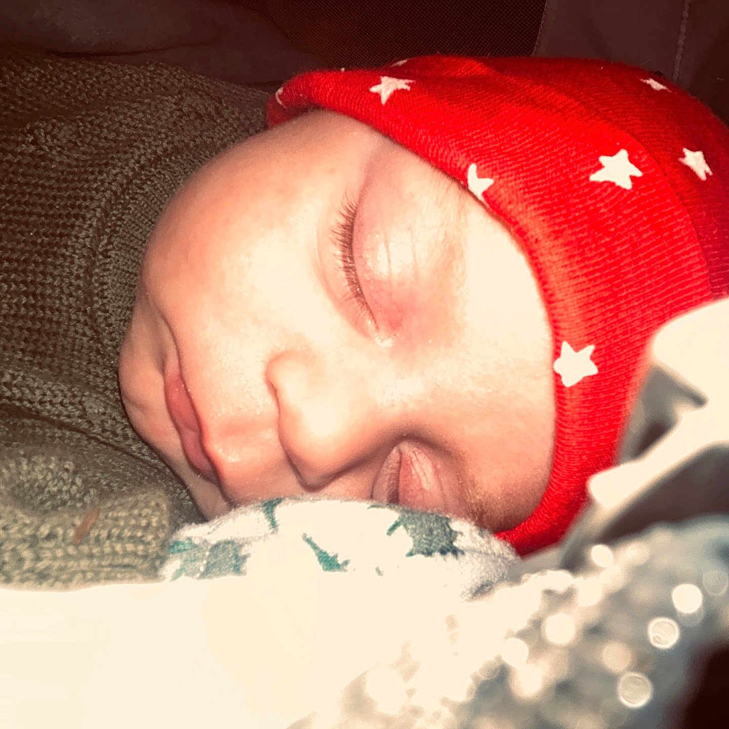 Kholtin is registered to the contest to win money with this photo: baby, blanket, child, close_up, cozy, cuddly, cute, eyelashes, face, indoors, infant, knitwear, peaceful, portrait, red_hat, rest, sleeping, soft, stars, warm
