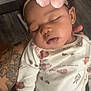 baby, sleeping, flower_headband, tattoo, onesie, animal_print, hand, indoor, person, cute, peaceful, child, infant, soft_lighting, portrait, skin, face, clothing, sleep, newborn