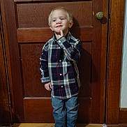 Colton is registered to the contest to win money with this photo: child, boy, plaid_shirt, jeans, boots, wooden_door, floor, indoor, standing, smiling, blond_hair, casual_clothing, thinking_pose, home, door_knob, wood_paneling, happy, cute, portrait, person