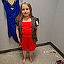 Maycee is registered to the contest to win money with this photo: child, girl, red_dress, gray_jacket, barefoot, fitting_room, blue_dress, hanger, floor, sneaker, tags, shopping, clothing, portrait, casual, indoor, curious, standing, tile_floor, wall