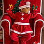 baby, child, christmas, santa_hat, red_clothing, plush_chair, gift_boxes, holiday, festive, pacifier, indoors, carpet, decorations, cute, portrait, holiday_outfit, celebration, smiling, seasonal, festivity