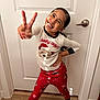 child, smiling, peace_sign, pajamas, red_pants, white_shirt, door, wood_floor, indoor, happy, playful, holiday_theme, bear_graphic, long_hair, light_pattern, footwear, socks, posing, cute, home
