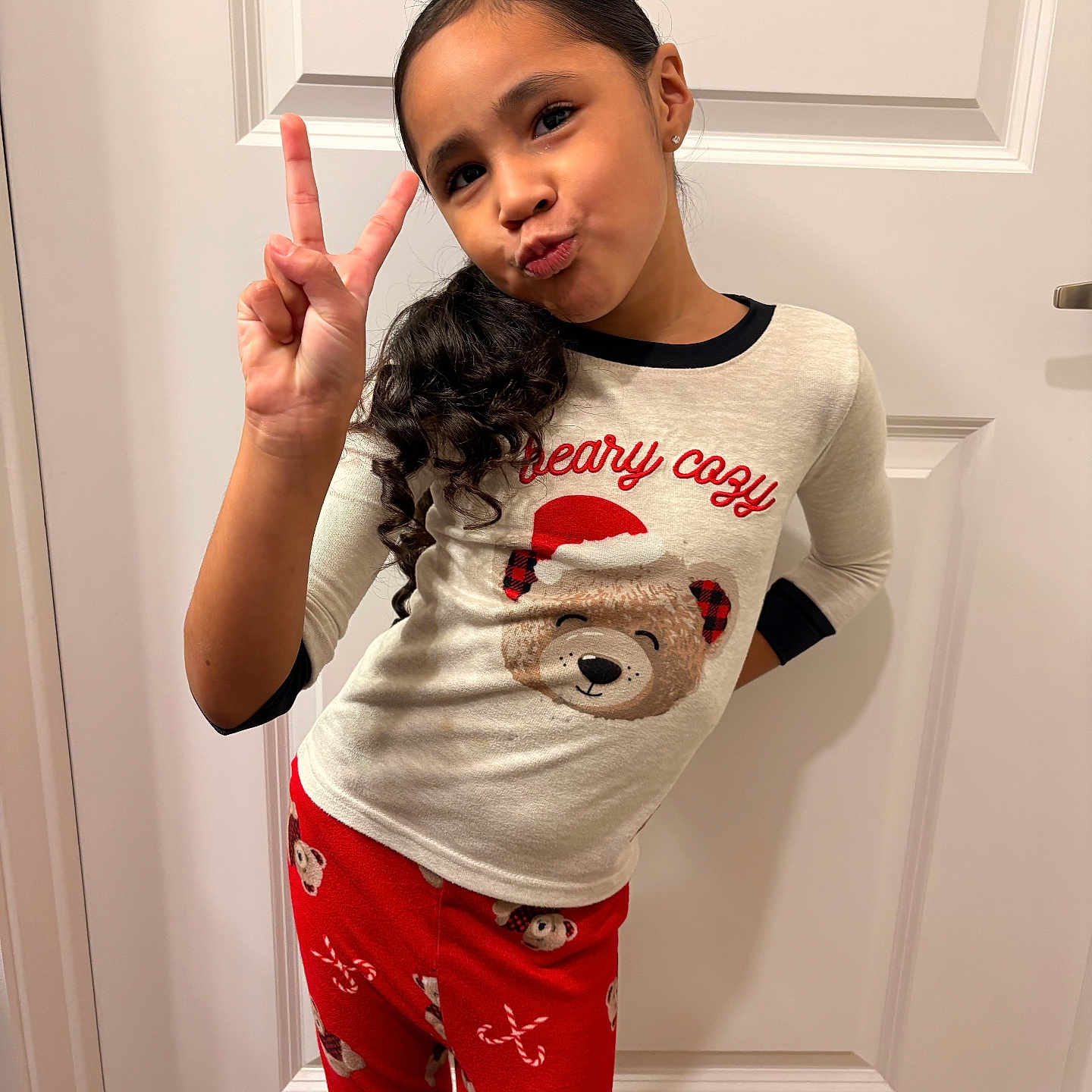 Jadiah joined the competition — help win amazing prizes! bear_graphic, casual, child, curly_hair, cute, door, festive, girl, happy, holiday, indoors, long_sleeves, pajamas, peace_sign, portrait, posing, red_pants, smile, white_top, youth