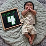 baby, infant, child, smiling, clothing, chalkboard, month, number, soft_mat, texture, wooden_frame, lying_down, cute, happy, indoors, hands, feet, portrait, young, comfortable