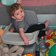 Charlie joined the competition — help win amazing prizes! toddler, child, high_chair, toys, stuffed_animals, playroom, curious, sitting, striped_shirt, black_pants, bare_feet, plastic_bottle, remote_control, colorful, indoor, baby, face, hand, foot, expression