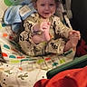 toddler, child, baby_rocker, pajamas, smile, happy, indoor, toy, blanket, foot, hand, face, curly_hair, seated, colorful, patterned_clothing, plush_toy, infant, cozy, playful