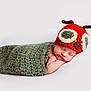 Teddy is registered to the contest to win money with this photo: newborn, baby, sleeping, knitted_wrap, crochet_hat, red_hat, green_wrap, antennas, cute, resting, soft_surface, infant, cozy, portrait, peaceful, child, headwear, sleep, baby_hat, closeup