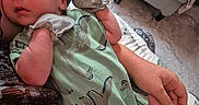 Nathan is registered to the contest to win money with this photo: adult_arm, baby, blanket, blue_hat, closeup, comfort, curious_expression, footwear, green_onesie, hand, holding, homedecor, indoor, infant, mittens, patterned_clothing, portrait, resting, rug, soft_toys