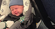 Nathan joined the competition — help win amazing prizes! baby, infant, car_seat, blue_hat, sleeping, cushion, patterned_fabric, seatbelt, carrying_handle, indoor, carpet, chair_leg, newborn, child, cute, cozy, smiling, clothing, person, portrait