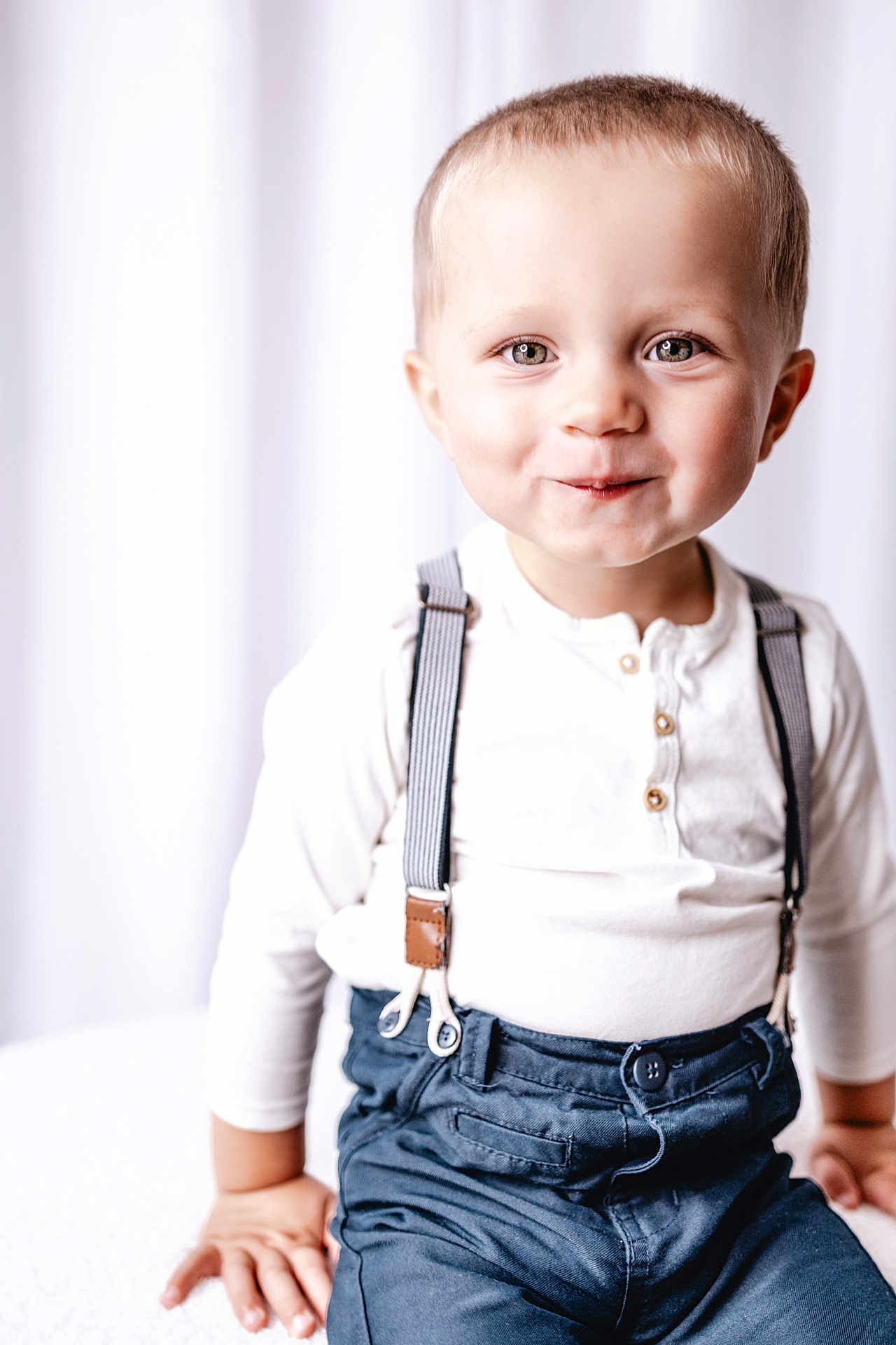 Raphaël participe au concours pour gagner de l'argent avec cette photo : child, toddler, portrait, smile, suspenders, white_shirt, blue_pants, indoor, studio, curtains, hands, eyes, blond_hair, cute, fashion, buttoned_shirt, sitting, closeup, soft_lighting, high_key