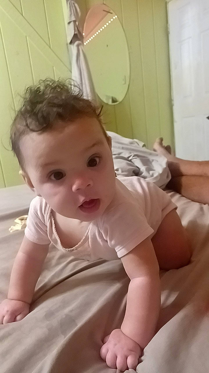 Josephine is registered to the contest to win money with this photo: abdomen, baby, baby_products, baby_toddler_clothing, cheek, chest, child, comfort, dress, flooring, happy, head, human_body, human_leg, iris, linens, person, room, skin, surprise