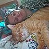 person, cat, orange_tabby, blanket, indoor, bedroom, portrait, sleeping_cat, cozy, resting, cute, animal, pet, human, casual, colorful_background, cartoon_wall, headwear, smiling, relaxing