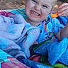 child, toddler, smiling, blanket, snack, outdoor, nature, trees, dirt, colorful, happy, person, face, clothing, playful, young_child, expression, cozy, relaxed, daytime