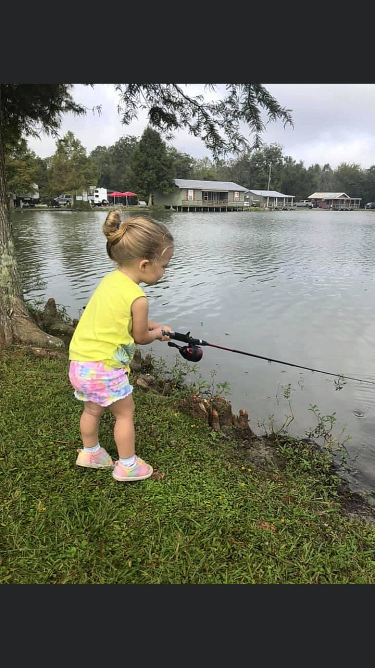 Addilyn is registered to the contest to win money with this photo: angling, bank, casting_fishing, cloud, fishing_reel, grass, lake, leaf, leisure, natural_environment, people_in_nature, person, plant, recreation, shorts, sky, summer, toddler, tree, water