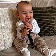 Leighton joined the competition — help win amazing prizes! baby, cheerful, child, clothing, couch, cozy, cute, happy, holding_object, home, indoor, infant, overalls, person, pillows, portrait, seated, small_child, smiling, white_socks
