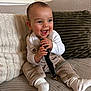 baby, cheerful, child, clothing, couch, cozy, cute, happy, holding_object, home, indoor, infant, overalls, person, pillows, portrait, seated, small_child, smiling, white_socks