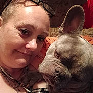 Smokey joined the competition — help win amazing prizes! woman, dog, french_bulldog, pet, face, glasses, indoor, couch, snuggling, closeup, paw, casual_clothing, portrait, home, relaxed, brown_hair, necklace, expression, animal, companion