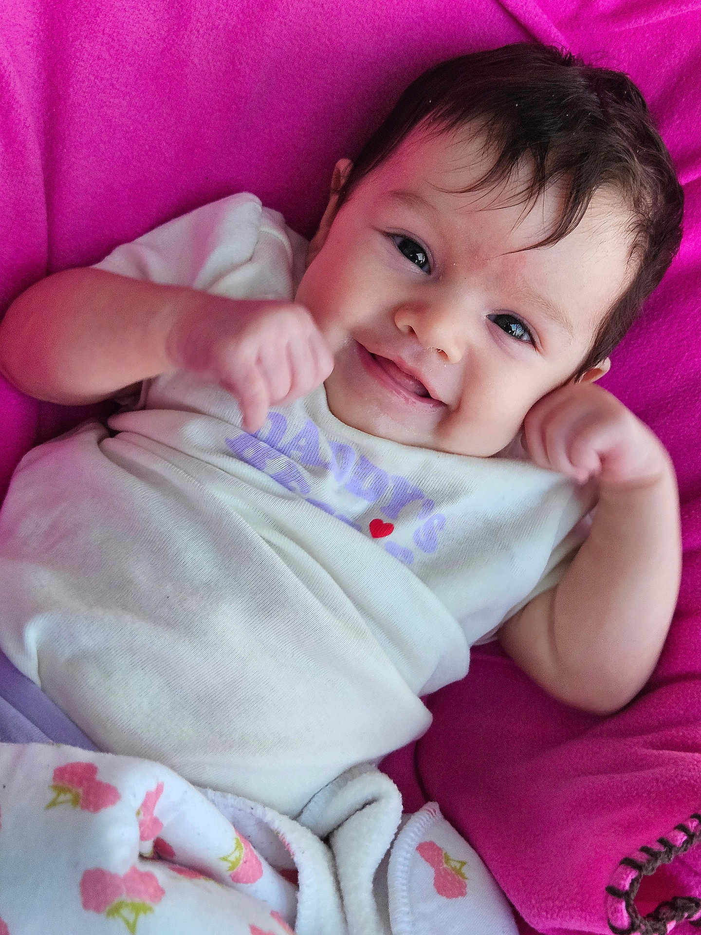Addilyn is registered to the contest to win money with this photo: baby, infant, smile, face, eyes, hair, cheeks, onesie, heart, pink_blanket, blanket, bedding, hands, fist, newborn, portrait, closeup, lying_down, cute, happy