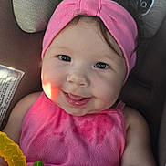 Ellie is registered to the contest to win money with this photo: baby, child, smiling, pink_headband, pink_clothing, toy, car_seat, infant, cute, happy, young_child, face, hand, portrait, seatbelt, indoor, closeup, childhood, adorable, playful