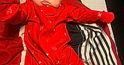 Macaya is registered to the contest to win money with this photo: arms_outstretched, baby, bed, child, cozy, cute, face, home, indoors, infant, lying_down, person, pillow, plush, red_onesie, resting, sleepwear, smiling, soft_lighting, striped_bedding