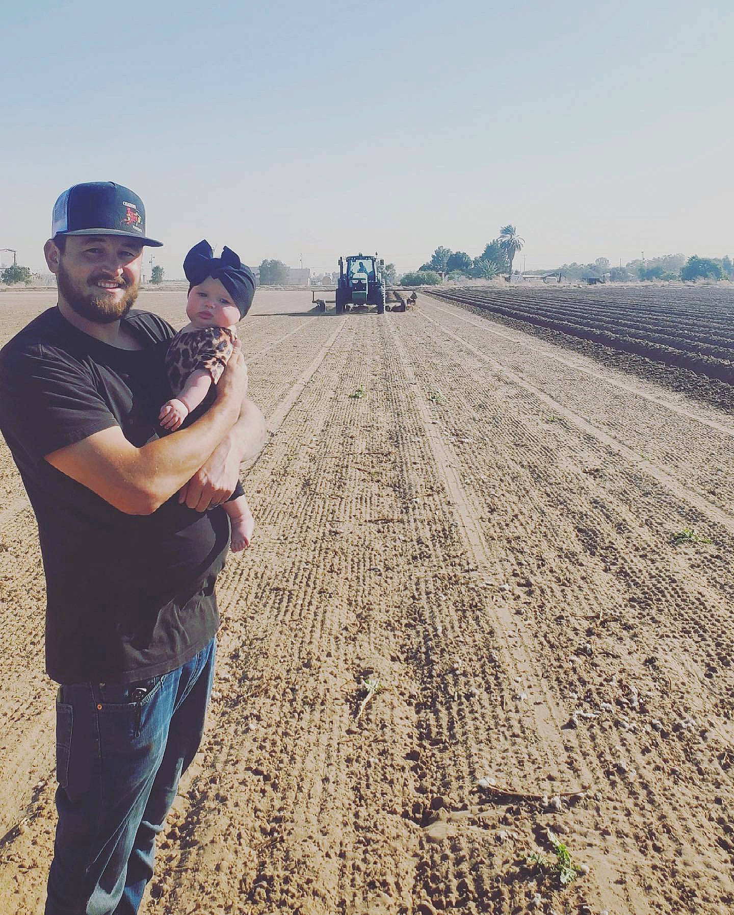 Blair is registered to the contest to win money with this photo: agriculture, baseball_cap, cap, farmer, farmworker, field, gesture, grass, happy, hat, headwear, horizon, joy, landscape, people_in_nature, person, sky, soil, t_shirt, tire