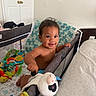 baby, child, playpen, toy, blanket, indoor, smile, happy, face, person, crawling, colorful, plush, diaper, furniture, bed, home, curly_hair, cute, infant