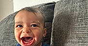 Enzo is registered to the contest to win money with this photo: baby, child, smiling, happy, blue_shirt, fox_design, couch, gray_couch, indoor, portrait, cute, young_child, textile_texture, patterned_background, infant, person, sitting, cheerful, closeup, casual_clothing