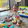 Enzo joined the competition — help win amazing prizes! baby, child, toy, carpet, high_chair, indoor, smile, play, floor, window, door, furniture, colorful, plastic_toy, person, happy, room, sitting, bright, daylight