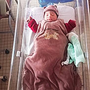 Noâm participe au concours pour gagner de l'argent avec cette photo : newborn, baby, sleeping, hospital, bassinet, blanket, hat, clothing, bed, infant, tiled_floor, person, indoors, soft_light, quiet, peaceful, wrapped, baby_bed, resting, cozy