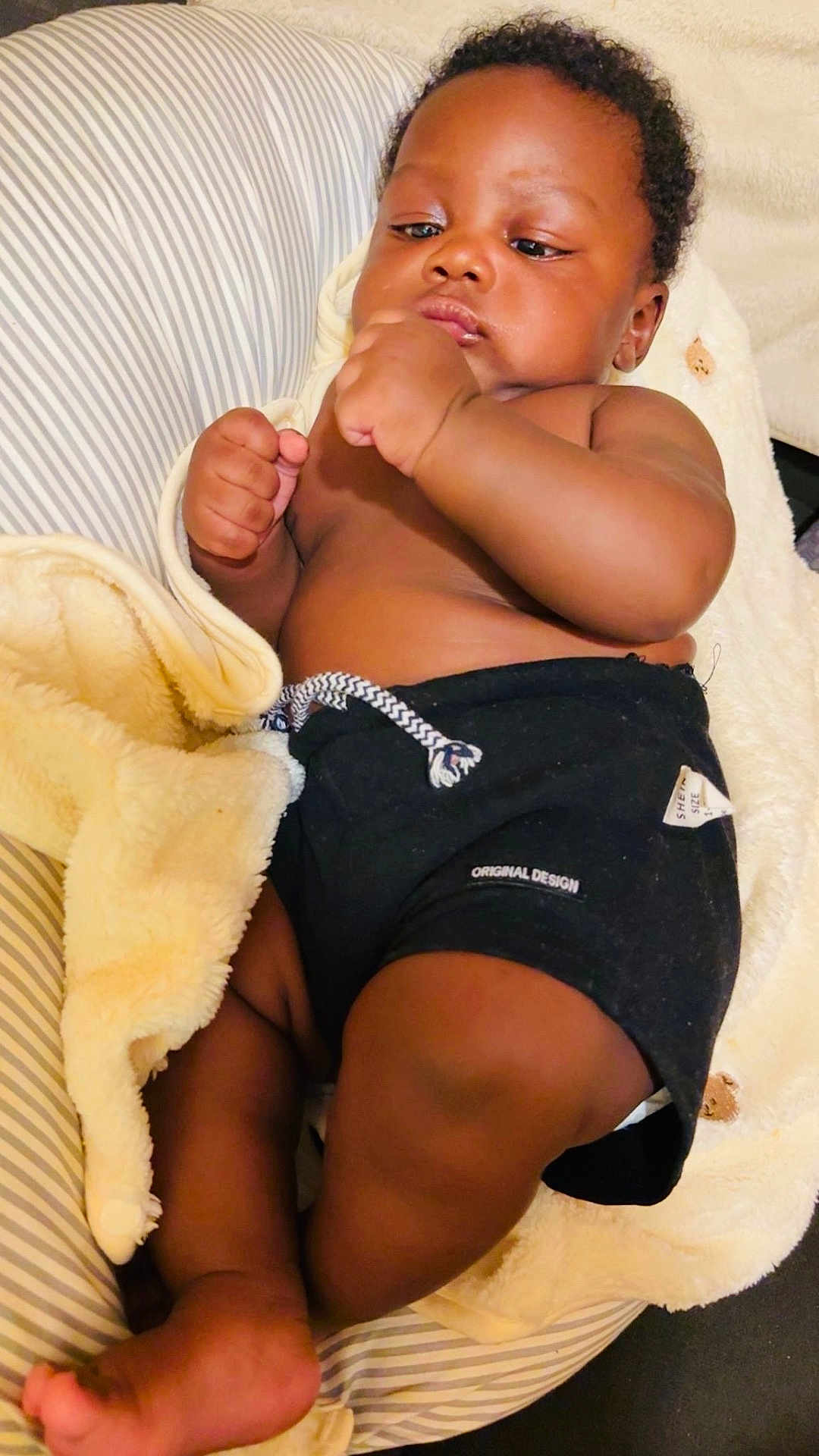 Kayron participe au concours pour gagner de l'argent avec cette photo : baby, infant, child, blanket, cushion, striped, clothing, black_shorts, skin, fist, comfort, relaxing, indoors, portrait, cute, young, person, resting, soft_texture, cozy