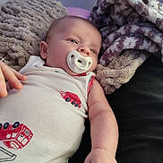 Hudson joined the competition — help win amazing prizes! baby, pacifier, infant, blanket, clothing, hand, face, person, sleepy, lying_down, soft_texture, indoors, couch, comfort, cute, child, skin, closeup, resting, white