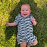 baby, grass, smiling, outdoor, child, happy, infant, clothing, patterned_clothes, barefoot, sunlight, nature, greenery, casual, cute, portrait, one_person, young_child, playful, summer