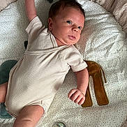 Liam a rejoint le concours — aidez-le/la à gagner de superbes lots ! baby, infant, onesie, play_mat, plush, dots, brown_letter, arm_up, curious, alert, soft_texture, indoor, child, person, cute, newborn, face, skin, head, lying_down