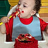 Zyaire is registered to the contest to win money with this photo: toddler, child, cake, red_frosting, messy, highchair, bib, food, eating, celebration, party, curly_hair, face, hand, plate, indoors, colorful_background, happy, young_child, birthday_cake
