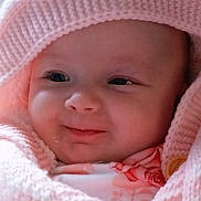 Aurora is registered to the contest to win money with this photo: baby, face, child, pink_blanket, knitted, smile, close_up, infant, cute, warm, apparel, soft_texture, portrait, young_child, expression, cozy, skin, headwear, wrapped, adorable