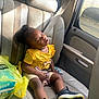 toddler, child, sleeping, car_seat, seatbelt, yellow_shirt, black_hair, pacifier, beads, sneakers, car_interior, window, sunlight, leather_seat, shopping_bag, relaxation, nap, cute, portrait, indoors