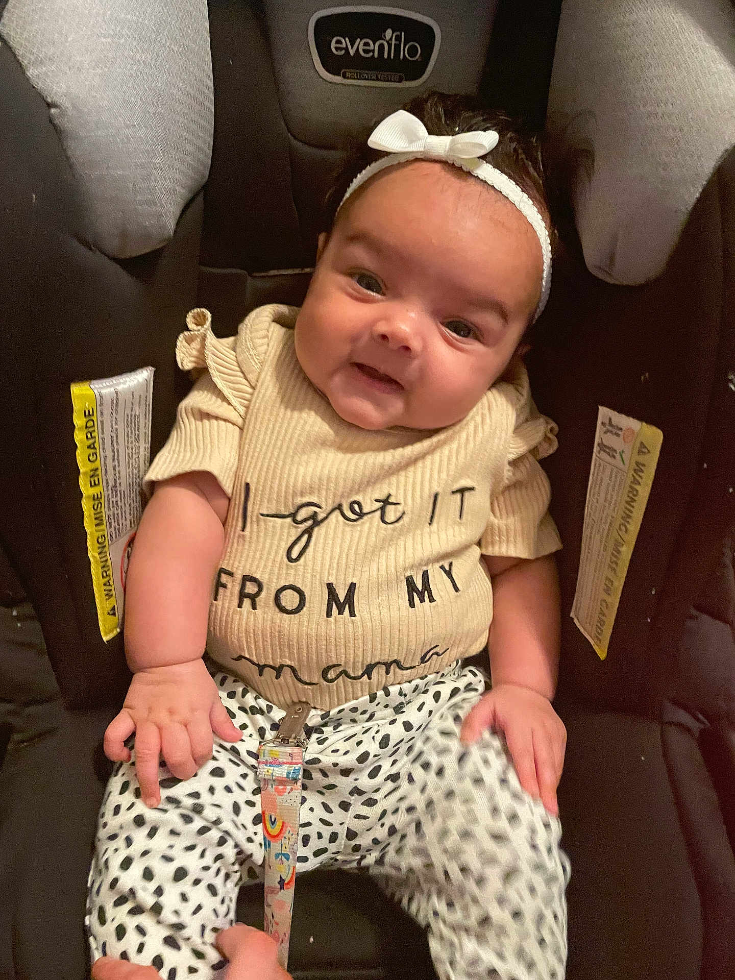 Leilani joined the competition — help win amazing prizes! baby, infant, child, car_seat, headband, smiling, clothing, white_bow, cute, person, infant_clothing, patterned_pants, seat, sitting, happy, young_child, cute_expression, indoors, child_seat, closeup