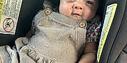 Leilani is registered to the contest to win money with this photo: baby, infant, car_seat, clothing, dress, button, face, hand, person, seat, safety_label, indoor, cute, child, young, portrait, expression, comfort, soft_lighting, closeup