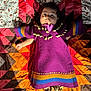 baby, child, purple_dress, shell_decorations, quilt, patchwork, colorful, moccasins, footwear, indoor, portrait, laying_down, wide_eyes, curious_expression, fabric, pattern, textile, hand, face, person