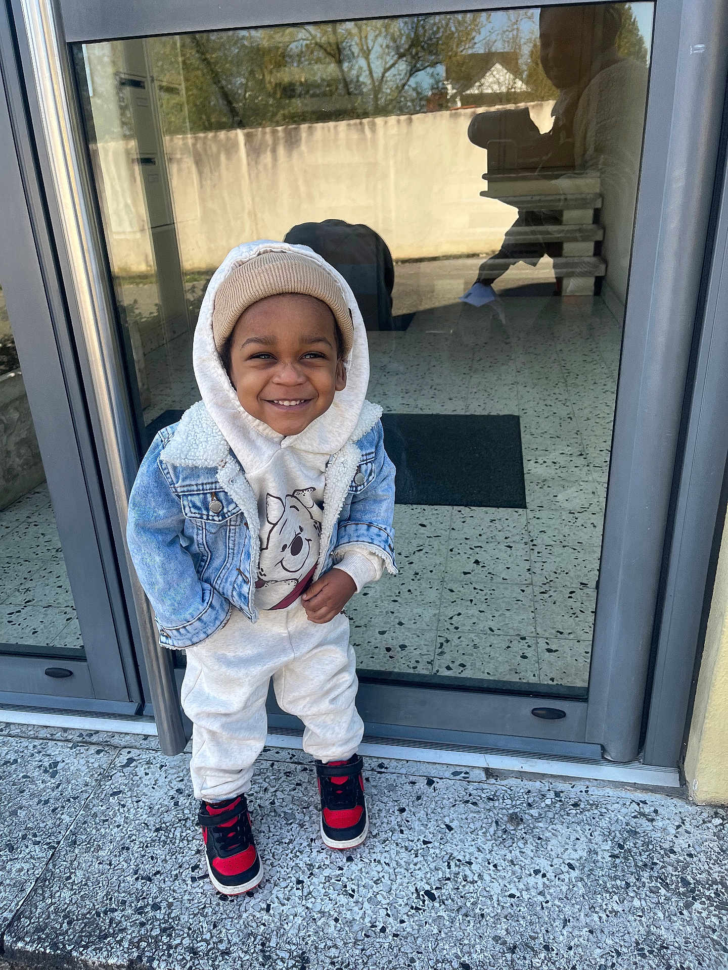 Tyler-Isaac participe au concours pour gagner de l'argent avec cette photo : beanie, casual_clothing, child, concrete, denim_jacket, floor, glass_door, happy, hoodie, outdoor, person, portrait, reflection, sidewalk, smiling, sneakers, standing, toddler, urban, winter_wear