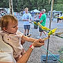 Kailyana joined the competition — help win amazing prizes! child, toddler, person, adult, bird, budgerigar, aviary, cage, feeding, stick, outdoor, people, fence, nature, greenery, animal, hand, wristband, curious, interaction