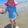 toddler, child, beach, sand, water, pacifier, sunhat, blue_shirt, striped_skirt, holding_hand, white_shoes, shadow, cloudy_sky, outdoor, summer, vacation, person, footwear, playing, closeup