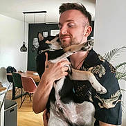 Riley joined the competition — help win amazing prizes! affection, black_dog, casual_clothing, chair, dog, happy, holding, home, human_animal_interaction, indoor, love, man, modern_interior, pet, plant, portrait, smile, table, tattoo, wooden_floor