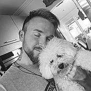Muffin joined the competition — help win amazing prizes! man, dog, pet, hug, affection, indoor, black_and_white, beard, curly_hair, tattoo, casual_clothing, kitchen, window, natural_light, smile, close_up, portrait, cute, cozy, love