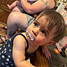 Violet joined the competition — help win amazing prizes! arm, baby, blurred_background, clothing, cream, curious, expression, face, family, hair, holding, indoor, person, seated, skin, table, tattoo, toddler, woman, wood