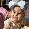 baby, child, headband, bow, smile, face, clothing, infant, cute, portrait, indoors, blanket, person, young_child, sitting, soft_lighting, apparel, expression, headwear, closeup